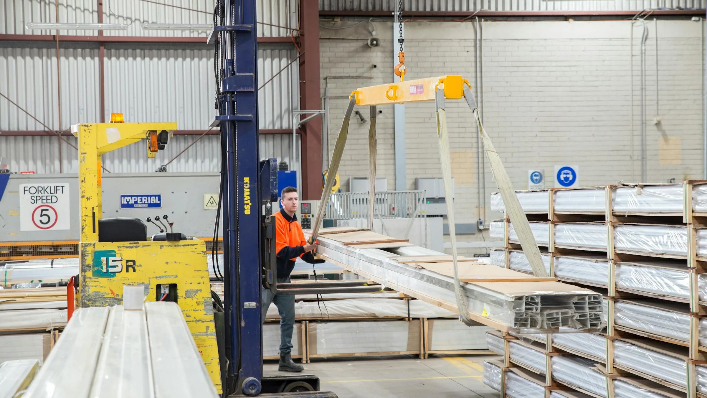 Forklift operator moving long industrial equipment in a warehouse